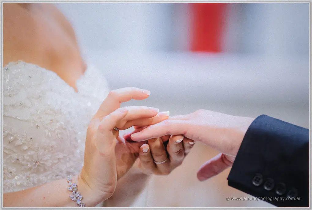 Macro of hands as Ashley eases the wedding ring onto Kristina's finger