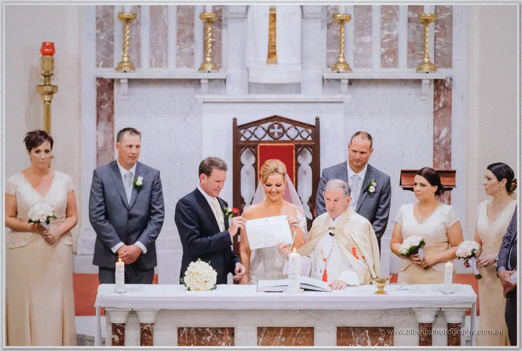 Ashley lifts the marriage certificate with Kristina as the priest looks on from the altar