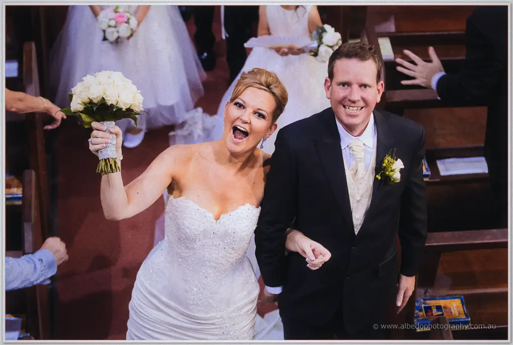 Kristina pumps her bouquet skyward mid-aisle as Ashley laughs beside her