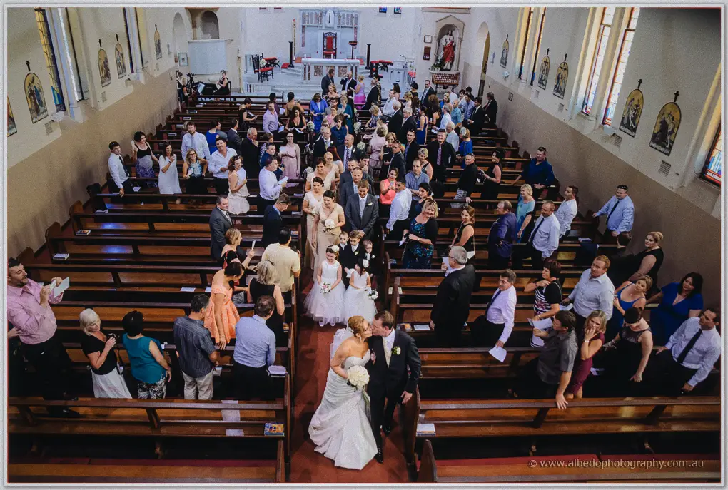 Loft view of the couple kissing in the aisle, guests turned all around them