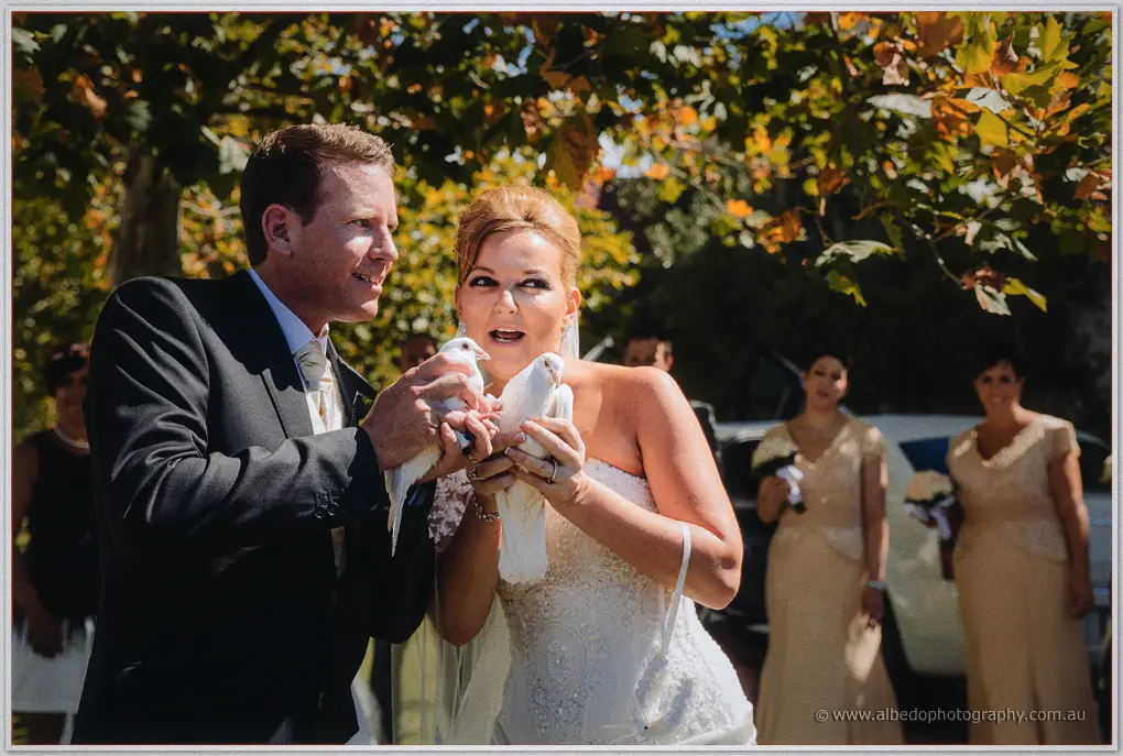 Kristina gapes as a dove flutters in her hands while Ashley steadies his own beneath autumn leaves