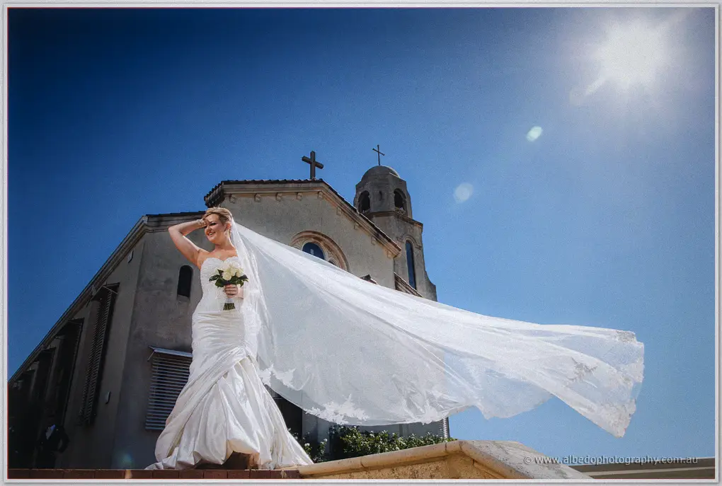 Kristina's veil whips sideways in the wind outside St Columba's under a deep blue sky