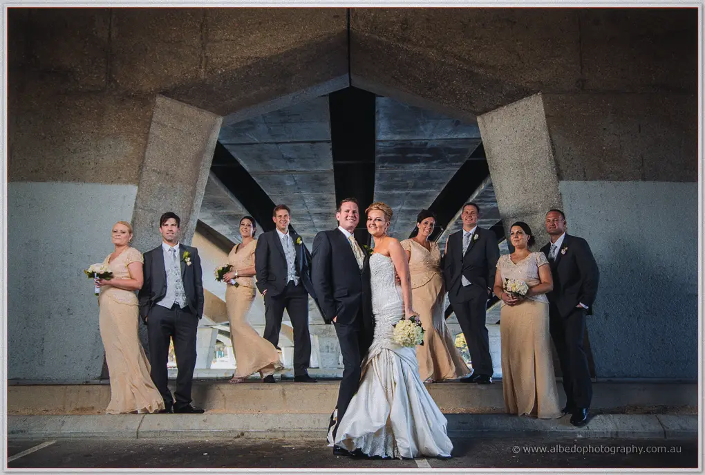 The wedding party lines up under a concrete bridge while Kristina and Ashley stand together in front