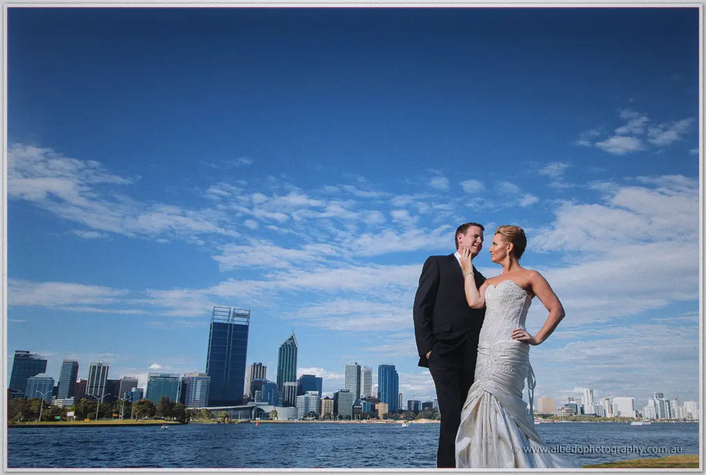 Kristina rests her hand on Ashley's cheek as they stand by the Swan River beneath a bright sky