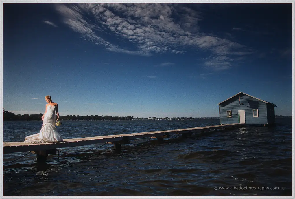 Kristina walks a long timber jetty toward the blue boat house on the Swan River at Crawley
