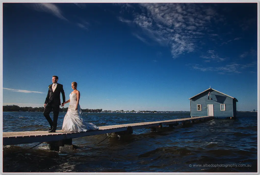 Kristina and Ashley walk hand in hand along the jetty past the blue boat house on the river