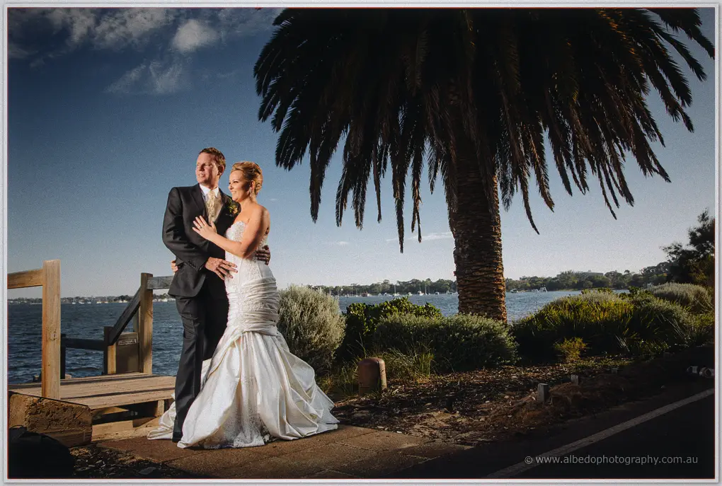 Kristina and Ashley embrace beneath a tall palm tree overlooking the river at sunset