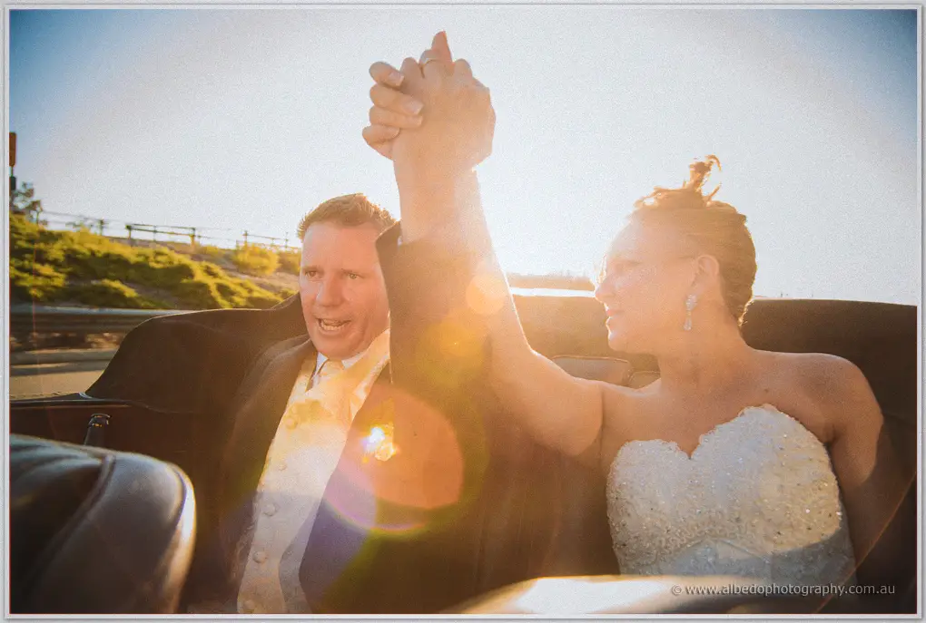 Ashley raises Kristina's hand triumphantly as sun flare washes over their convertible ride