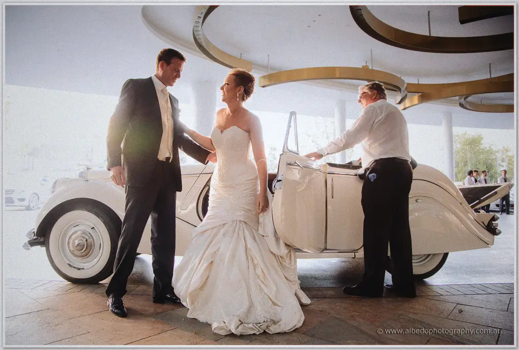 A chauffeur opens the door of a cream vintage car as Kristina and Ashley arrive at Crown