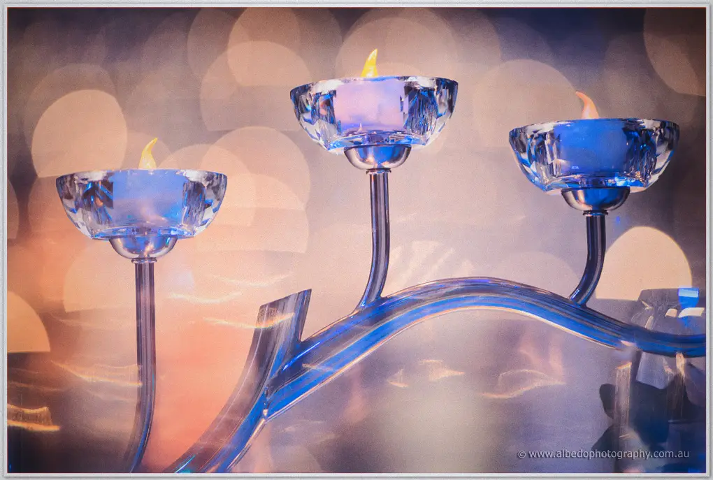 Blue crystal candle cups flicker on a curved stand against warm bokeh in the ballroom