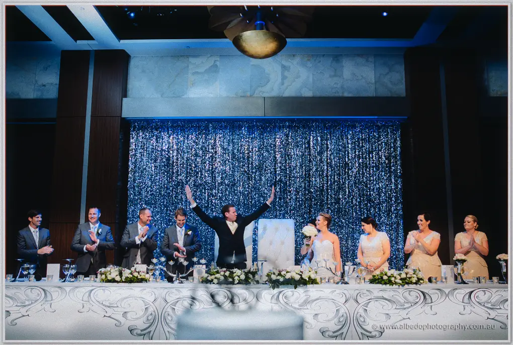 The full bridal table stands cheering beneath the sparkling curtain of the Astral Ballroom