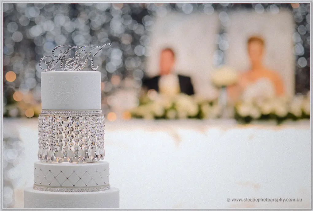 A crystal-draped white cake with an A and K monogram topper before the bridal table