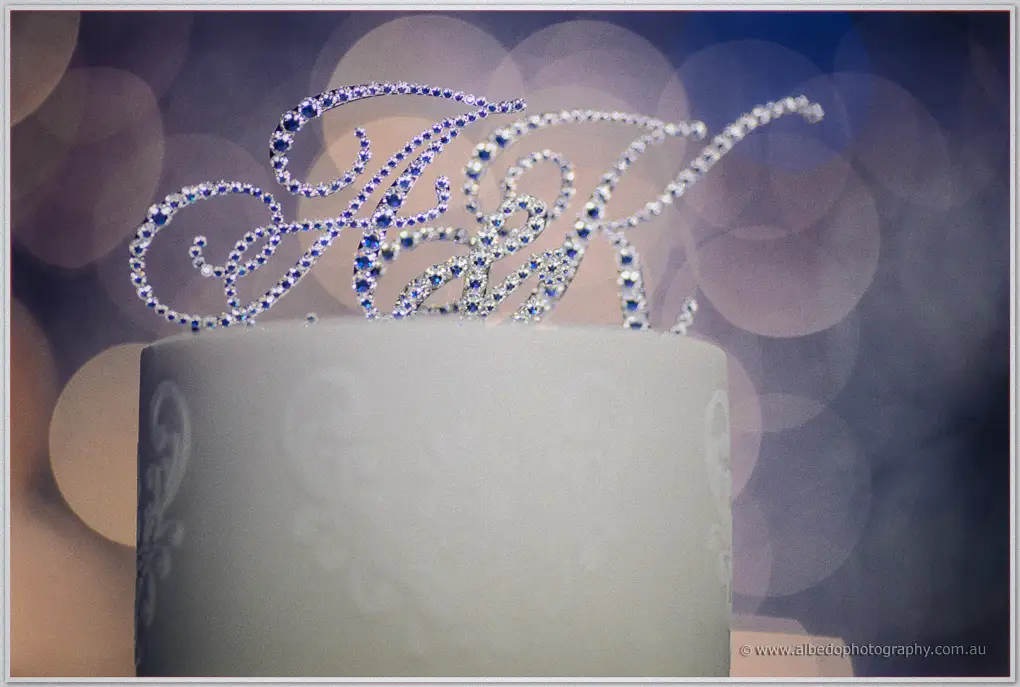 A rhinestone A and K topper crowns the white wedding cake in soft blue and gold light