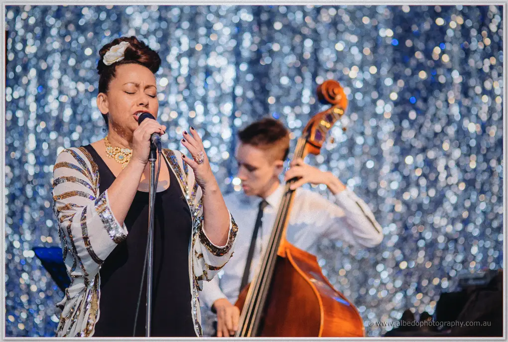 A sequinned vocalist sings with her double bassist against shimmering silver curtains