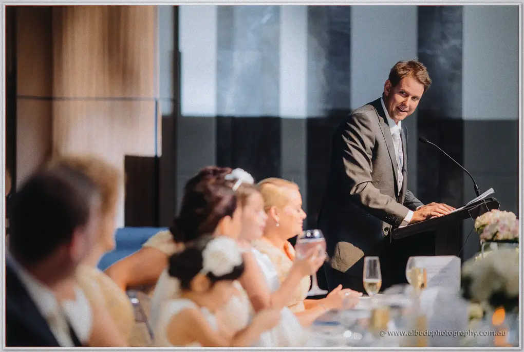 The best man delivers his speech as guests listen beside candles and blush blooms