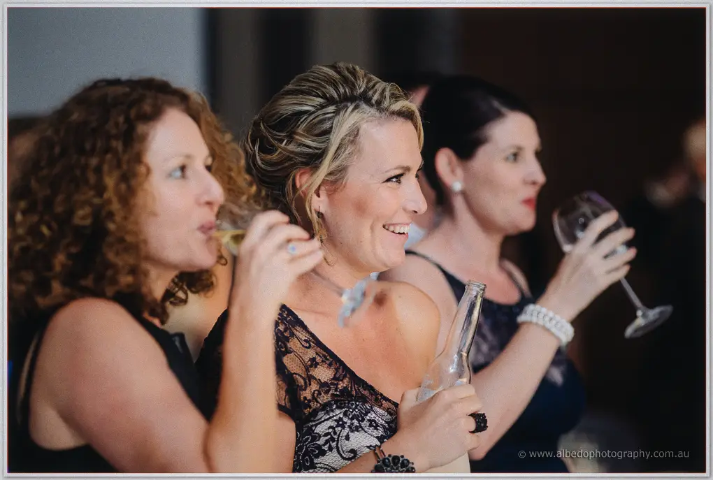 Guests in black lace sip wine and smile during the reception toasts