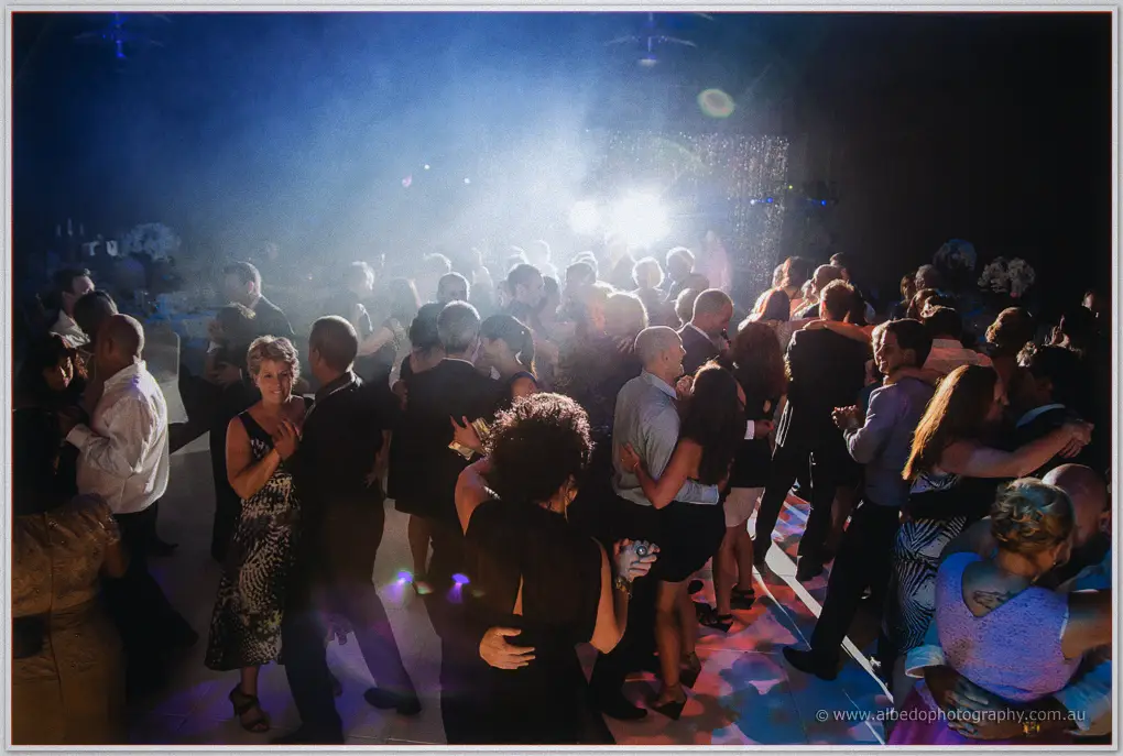 A packed dance floor of guests dancing through haze and colorful lights at the Crown wedding reception.