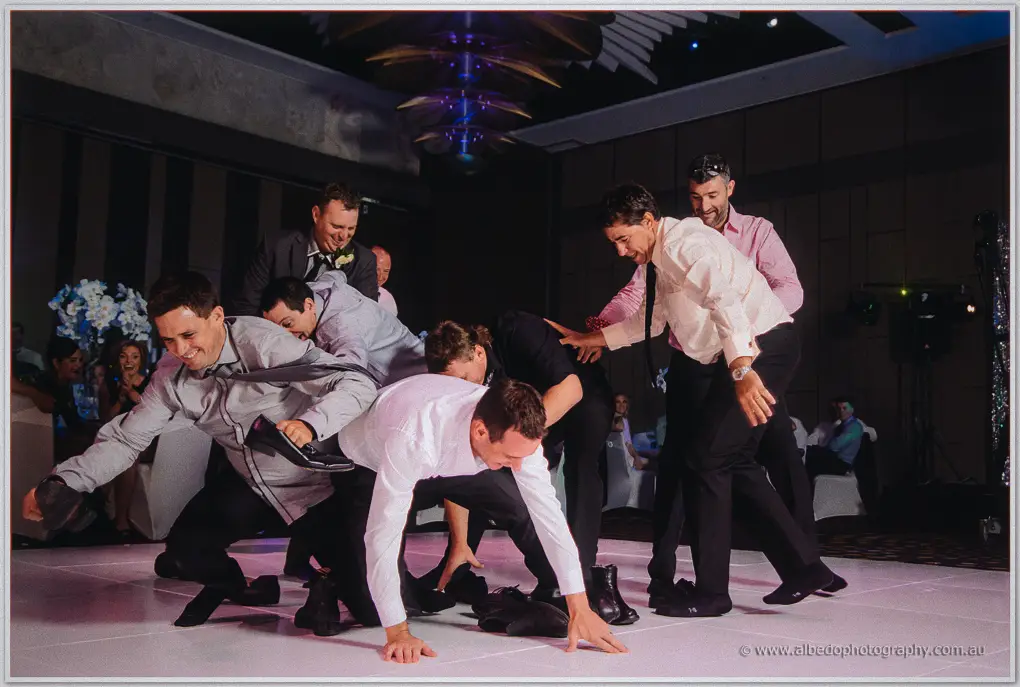 Groomsmen in shirts and ties tumble and clown together during a rowdy group dance at the wedding reception.