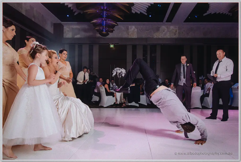 A groomsman breakdances upside down as Kristina and the flower girls watch open-mouthed with delight.