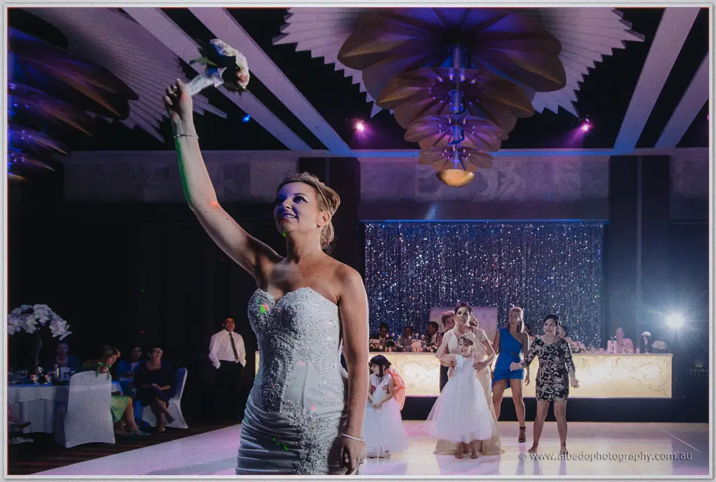 Kristina triumphantly raises her bouquet overhead before guests and flower girls at the Crown reception.