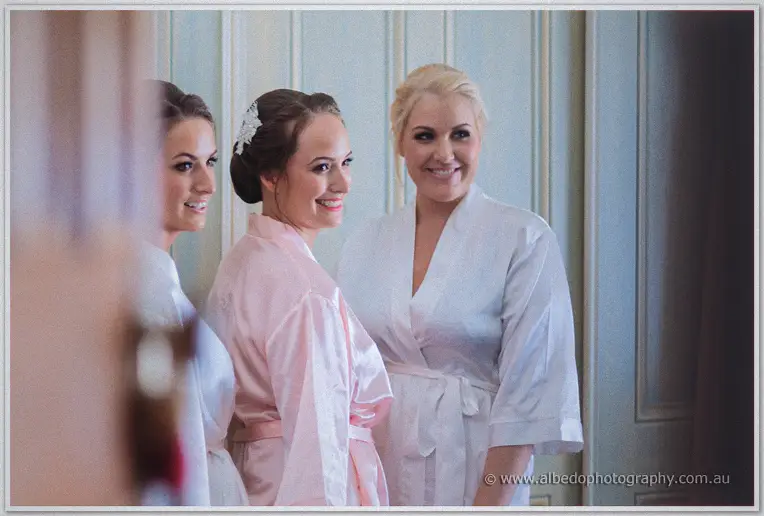 Katelyn grins over her shoulder in a pink robe while bridesmaids stand close behind her