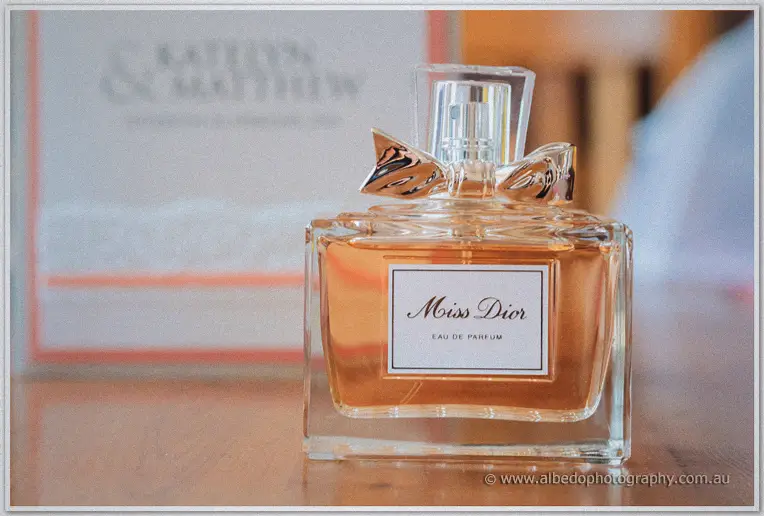 Perfume bottle glowing amber in window light beside the couple's personalised invitation