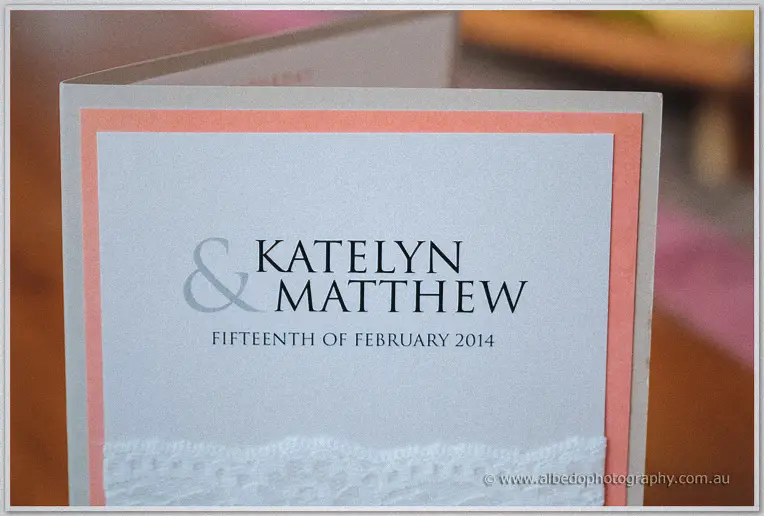Katelyn and Matthew's wedding invitation card with coral trim and a lace border detail