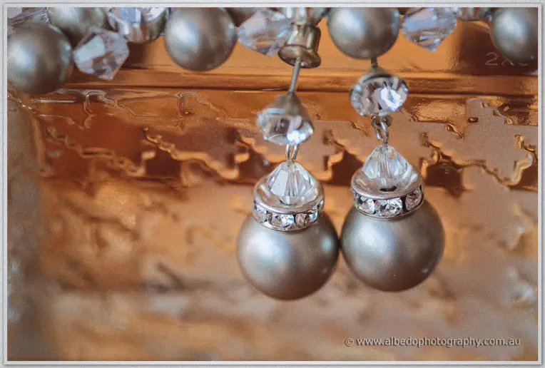 Pearl drop earrings with crystal accents hang against an ornate antique gold mirror