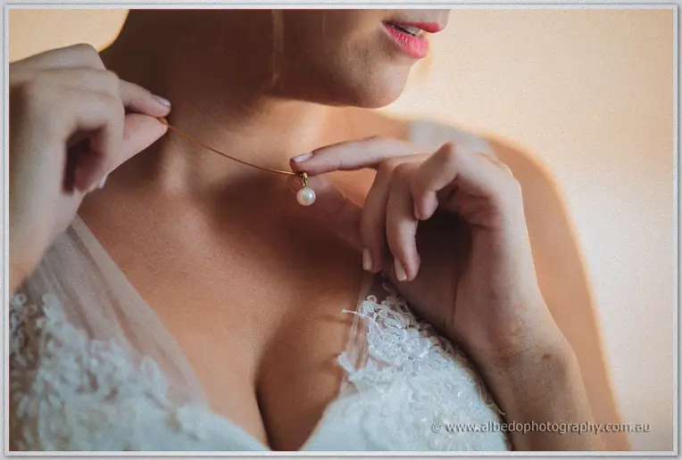 Close-up of Katelyn fastening a pearl pendant at the neckline of her lace gown