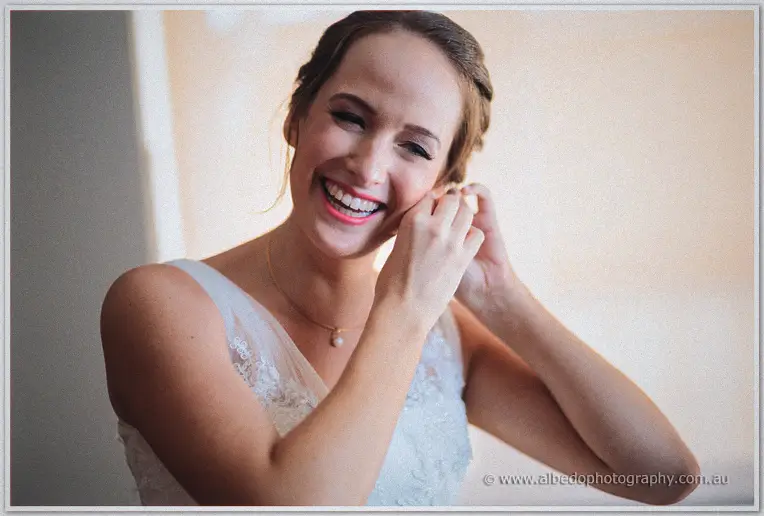 Katelyn laughs as she clips in an earring, updo and pearl necklace catching window light