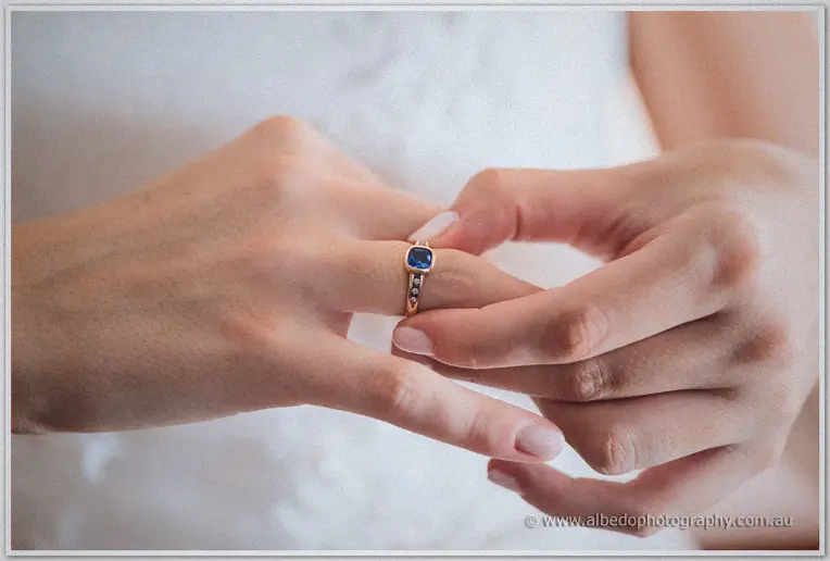 Katelyn's hands slip the sapphire engagement ring onto her finger over white lace