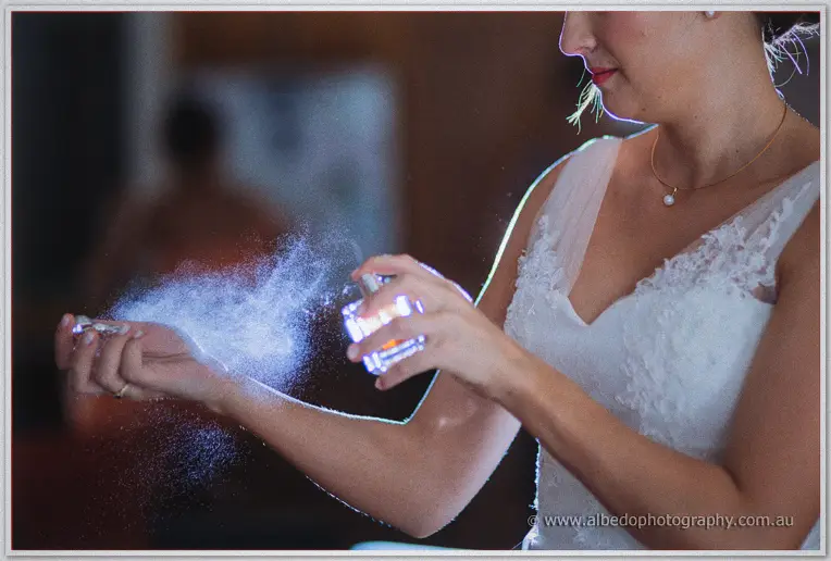 Katelyn sprays perfume into a mist above her wrist, veil and red lips rimmed in light