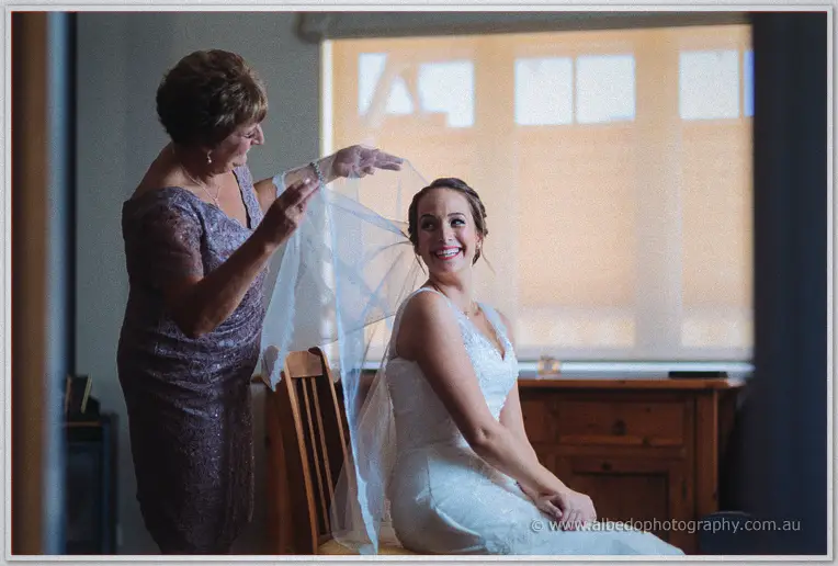 Katelyn's mother drapes the veil over her seated daughter's shoulders, both beaming