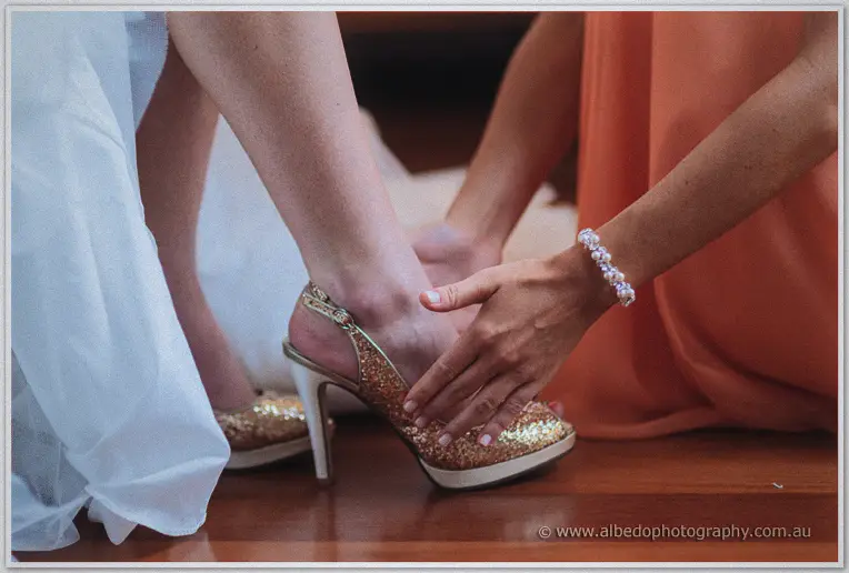 A bridesmaid steadies Katelyn's glittering gold heel as she dresses for the vintage Brookleigh wedding