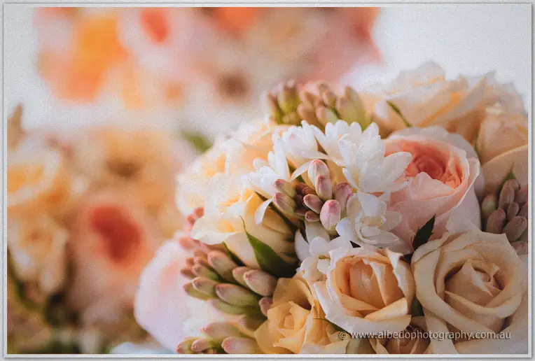 Soft window light warms peach roses and freesia in the bridal bouquet at Brookleigh