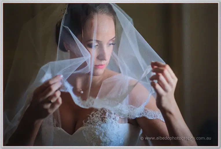 Katelyn lifts her lace-edged veil in soft window light before her Brookleigh wedding
