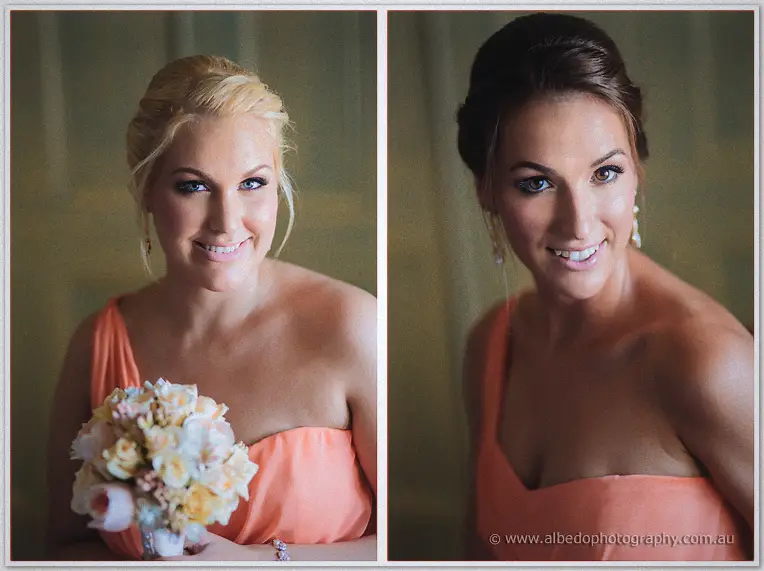 Two bridesmaids in coral dresses smile for portraits, one cradling her rose bouquet