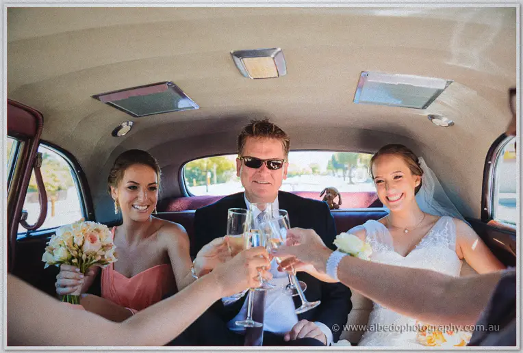 Katelyn and her father toast champagne in the back of the classic wedding car