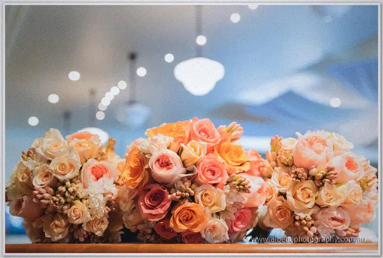 Three rounded bouquets of peach and apricot roses lined up beneath glowing pendant lights