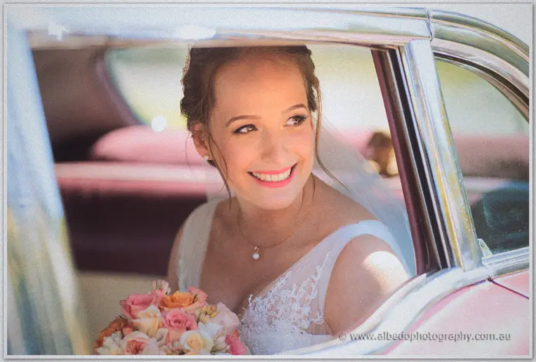 Katelyn grins from the vintage car window, her peach bouquet on her lap