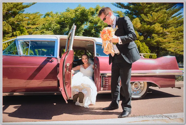 Katelyn laughs as Matt greets her stepping from the vintage car in bright sun