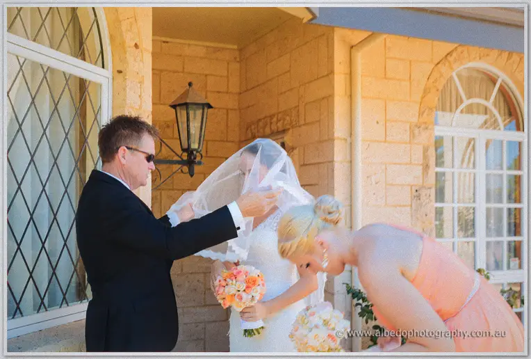 Katelyn's father settles her veil outside the limestone homestead before the ceremony