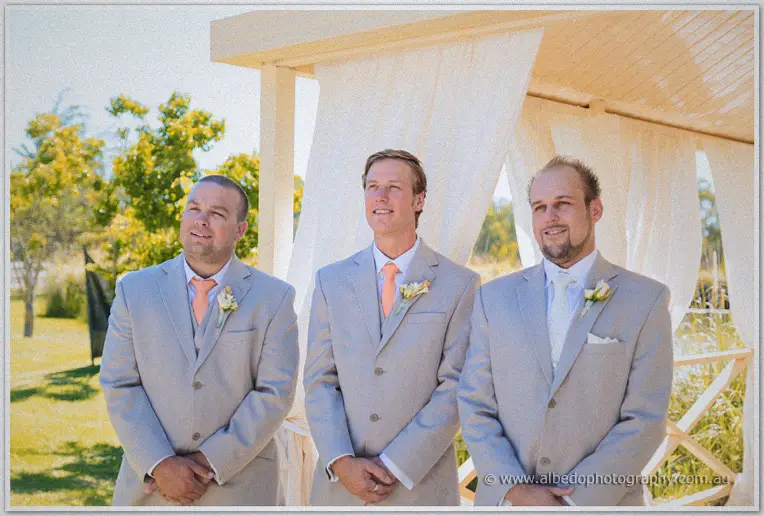 Matt's groomsmen wait by the white arbour in stone suits and peach ties