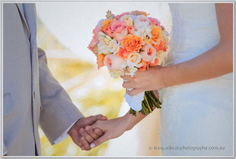 Katelyn and Matt clasp hands, her peach rose bouquet between them