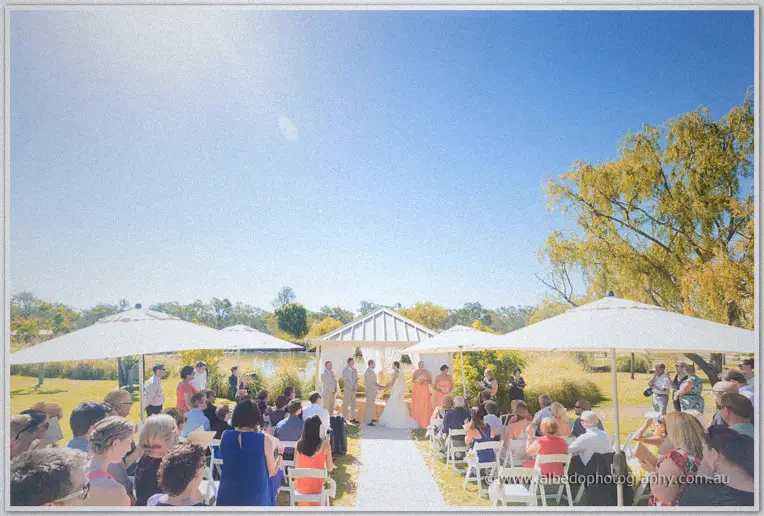 Guests fill white chairs beneath parasols for Katelyn and Matt's lakeside ceremony