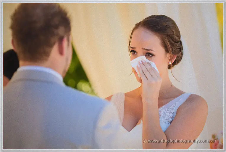 Katelyn dabs happy tears with a tissue during her lakeside vows at Brookleigh