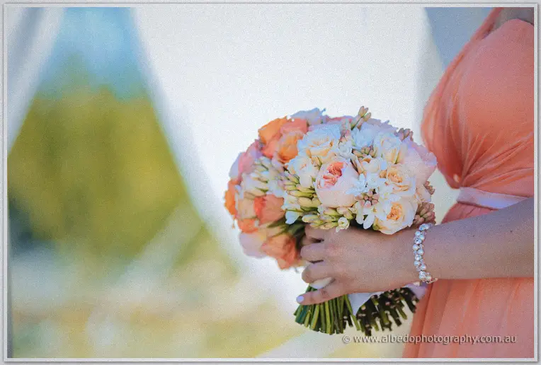 A bridesmaid holds her peach and cream rose posy in the arbour's shade