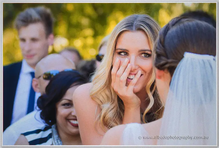 A blonde guest laughs behind her hand as she greets Katelyn after the ceremony