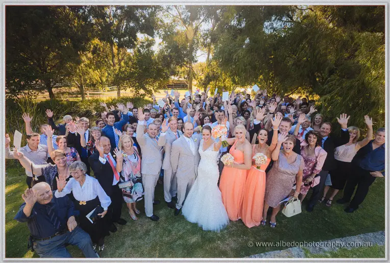 Every guest waves cheerfully around the newlyweds in a wide Brookleigh group shot