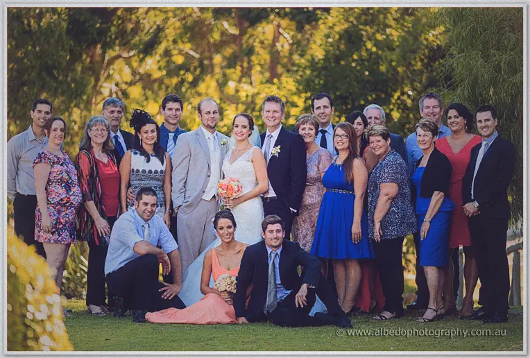 Family and friends crowd around the couple for a garden group photo at Brookleigh